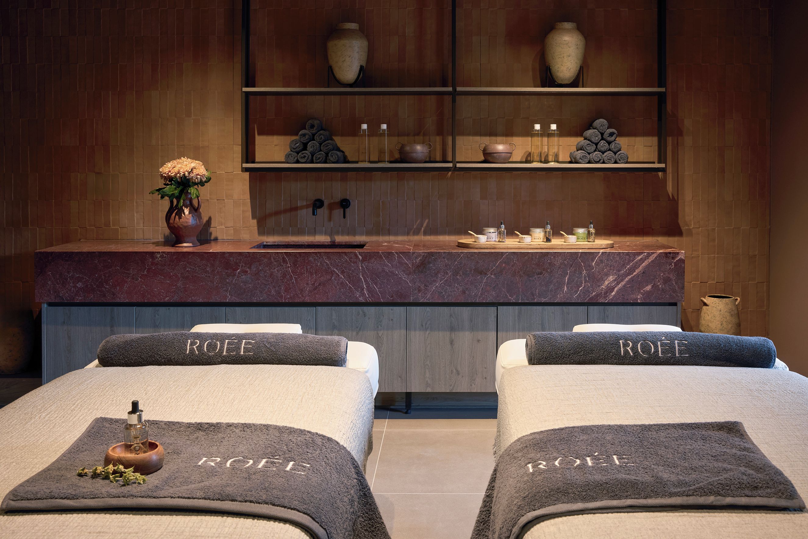 A spa room with two massage beds, a marble countertop, and shelves with toiletries and decorative items.