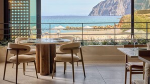 A balcony with a view of the sea and cliffs, furnished with chairs and a table.