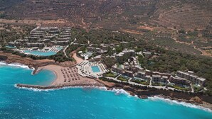 An aerial view of a coastal resort with multiple buildings, a beach, and a pool area.