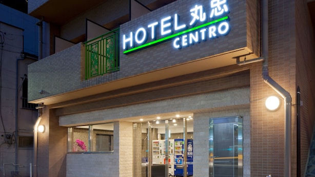 L’entrée d’un hôtel, avec une enseigne lumineuse au néon, des portes en verre et des distributeurs automatiques à l’extérieur.