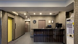 Un espace d’accueil d’hôtel comprenant un comptoir de réception, une horloge, un distributeur de billets et une porte avec une pancarte.