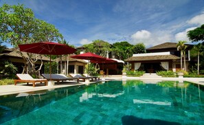 A pool area with lounge chairs and red umbrellas, surrounded by tropical vegetation and buildings. - Tamarind Exclusive Villa (Sattahip)