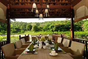 A dining area with wicker furniture, a table set for two, and a view of a lush green landscape. - Tamarind Exclusive Villa (Sattahip)