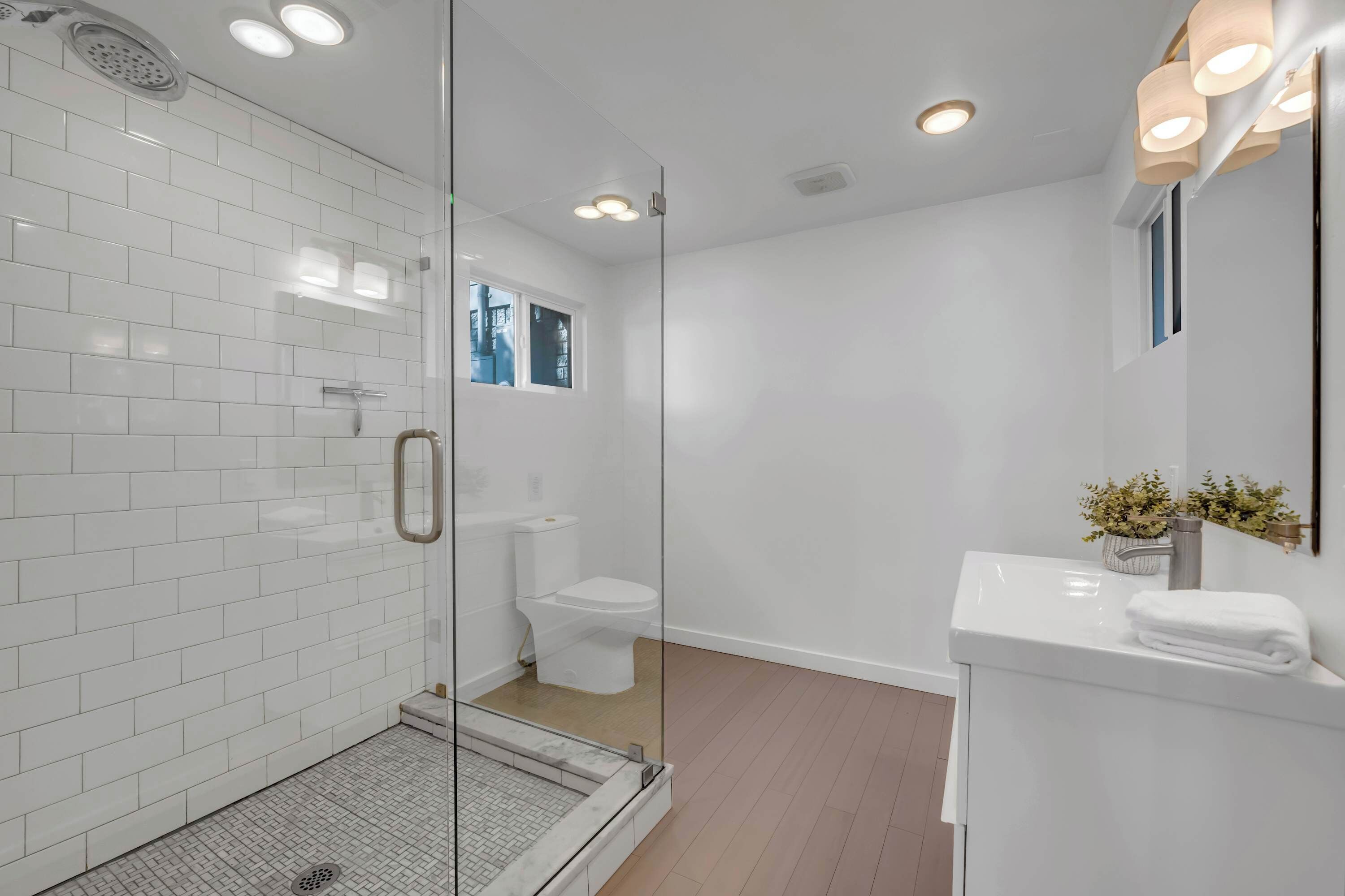 Een moderne badkamer met witte betegelde wanden, een douchecabine met glazen wanden, een toilet en een wastafel met een handdoek.