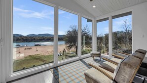 A spacious room with large windows offering a view of a beach and lake.