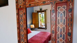 A room with a large mirror framed in ornate red and blue patterns, a bed with a red bedspread, and a window with a view of greenery outside. - Great Villa ideal for groups: swimming pool, wifi, air conditioning, sea view. (Frigiliana)