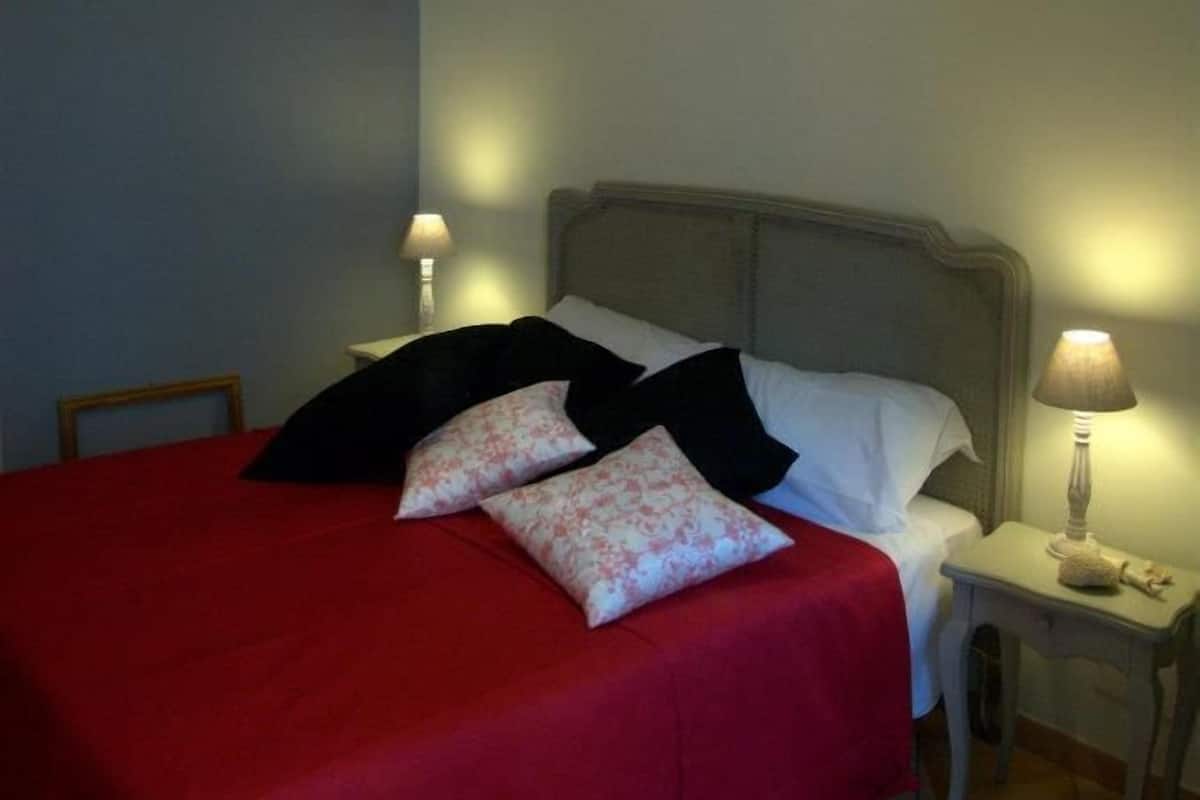 A neatly made bed with a red bedspread and black and white pillows, a bedside lamp, and a hanging light fixture.