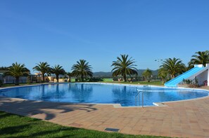 A large outdoor swimming pool with a blue slide, surrounded by palm trees and a clear sky. - Camping Resort & Bungalow Park Mas Patoxas (Pals)