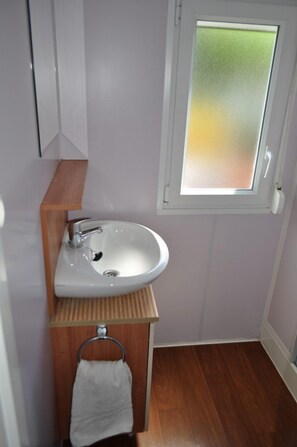 A small bathroom with a white sink, wooden vanity, and a window with frosted glass.