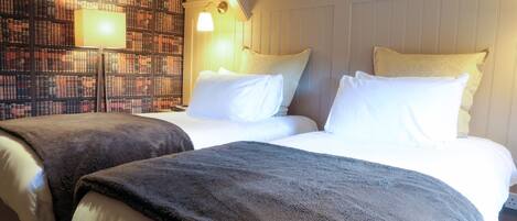 A hotel room with two beds, a bookshelf wall, and a lamp.