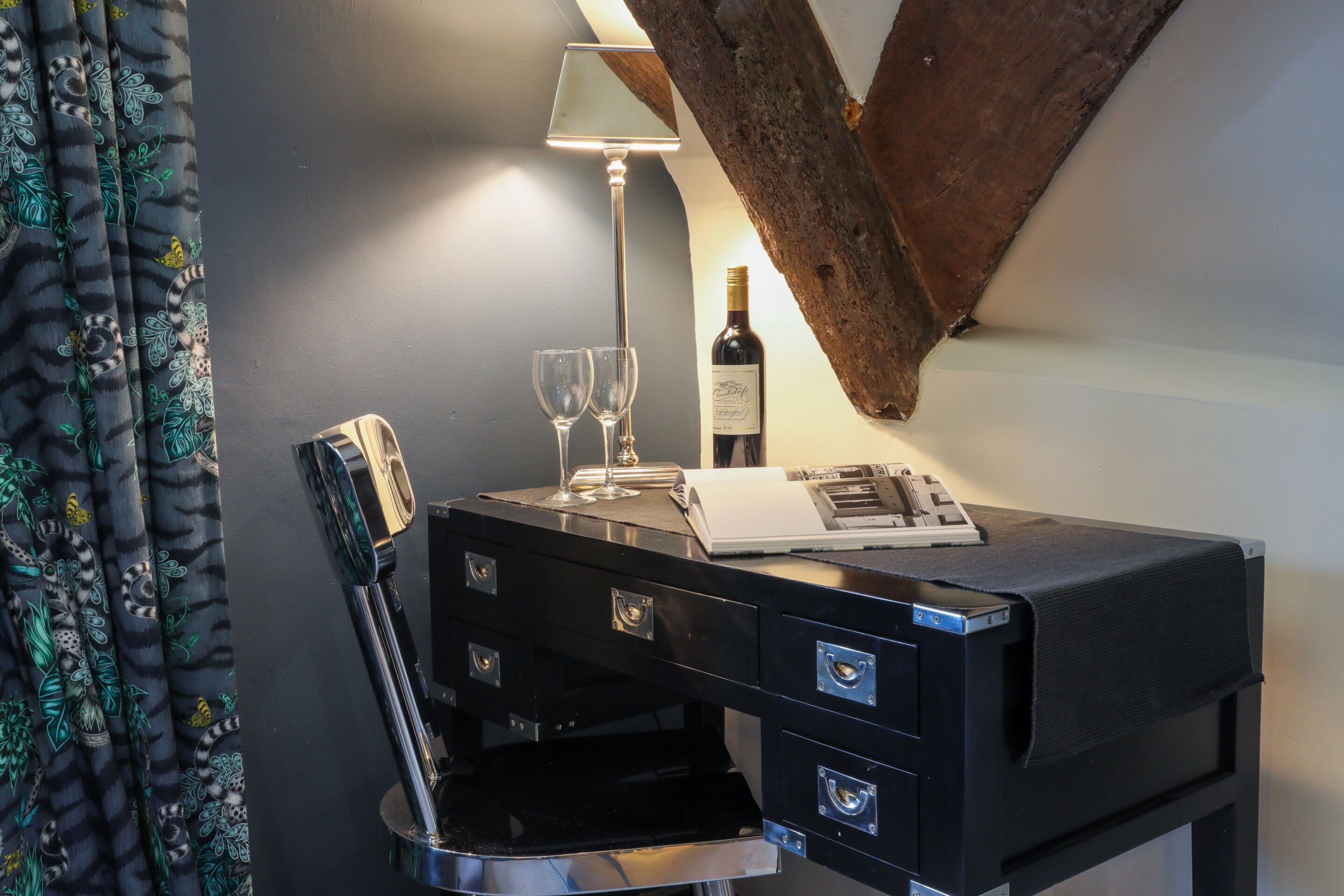 A black desk with a wine bottle, two glasses, and a lamp.