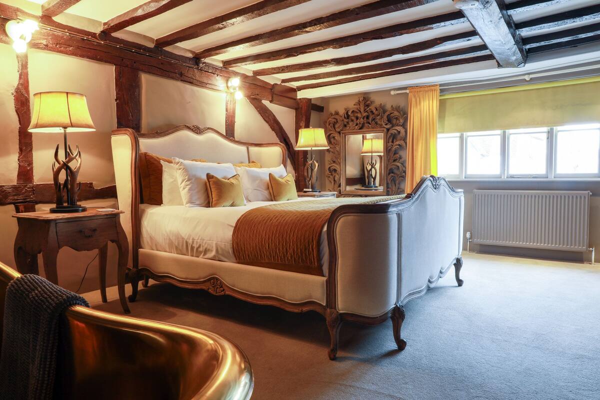 A traditional bedroom with a four-poster bed, two bedside tables, a large mirror, and a radiator.