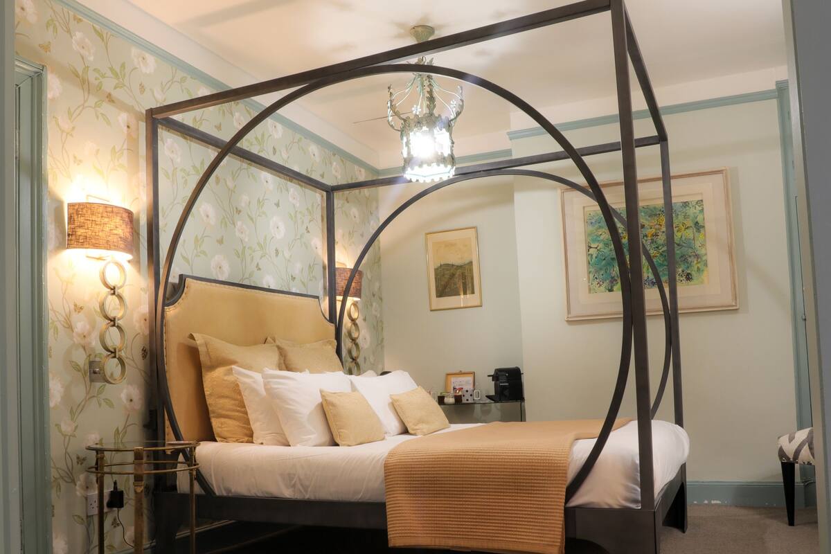 A four-poster bed with a canopy, a bedside table, a lamp, and a framed picture on the wall.