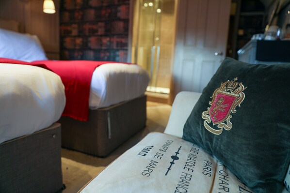 A hotel room with a bed, a sofa, and a decorative pillow with a crest. - The Kingsbury at No7 & No8 (Marlborough)
