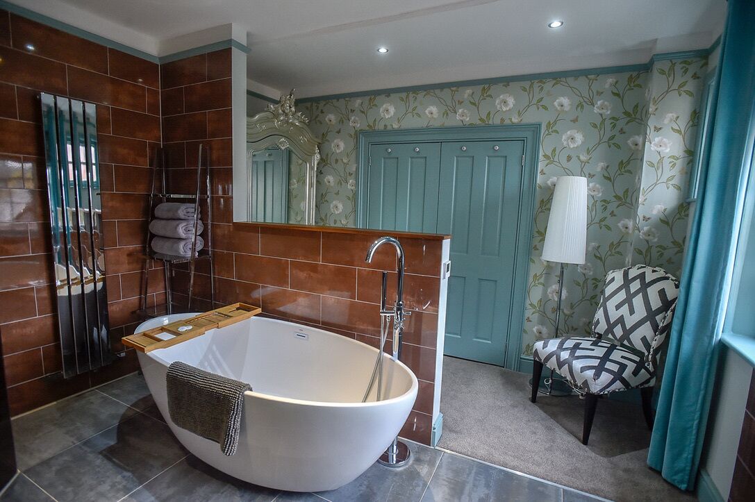 Une salle de bain avec une baignoire sur pieds, un porte-serviettes, une chaise et une porte recouverte d’un papier peint à motifs floraux.