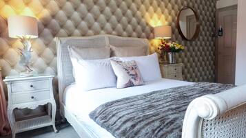 Una cama bien tendida con un edredón gris, un cabecero blanco y dos mesitas de noche con lámparas y un jarrón con flores.
