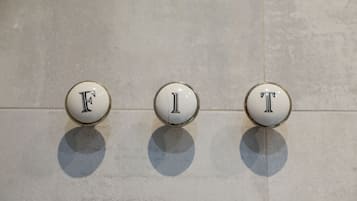 Trois boutons ronds et blancs, portant les lettres « F », « I » et « T », sont fixés sur un mur recouvert de carreaux.