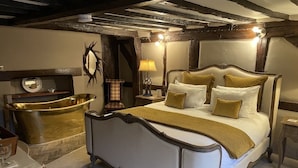 A bedroom with a large bed, a wooden headboard, a bedside table with a lamp, and a stone bathtub. - The Kingsbury at No7 & No8 (Marlborough)