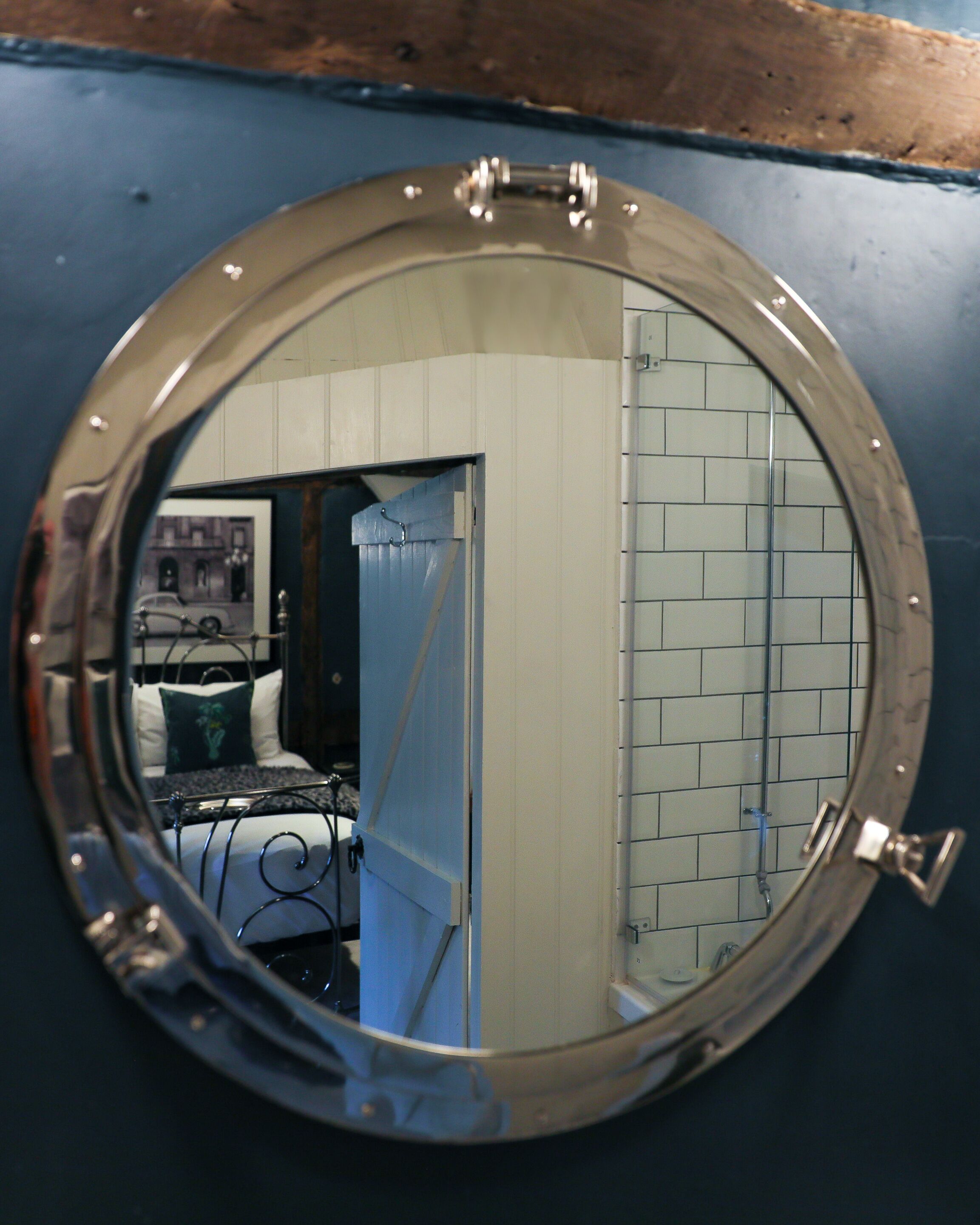 A round mirror with a metal frame reflecting a room with a bed, a door, and tiled walls.