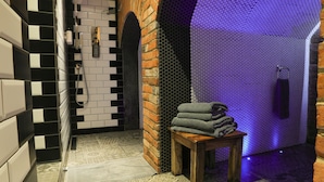 A bathroom with a tiled wall, a wooden bench with towels, and a shower area. - The Kingsbury at No7 & No8 (Marlborough)