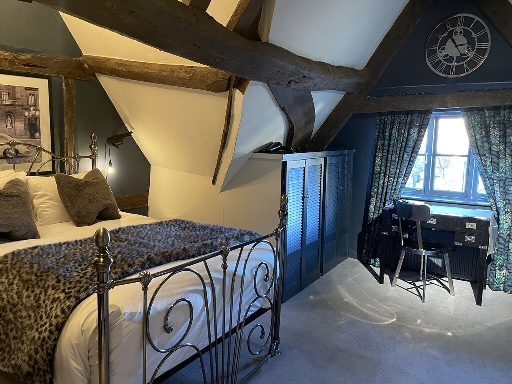 A bedroom with a bed, a desk, and a chair. There is a window with curtains and a clock on the wall.