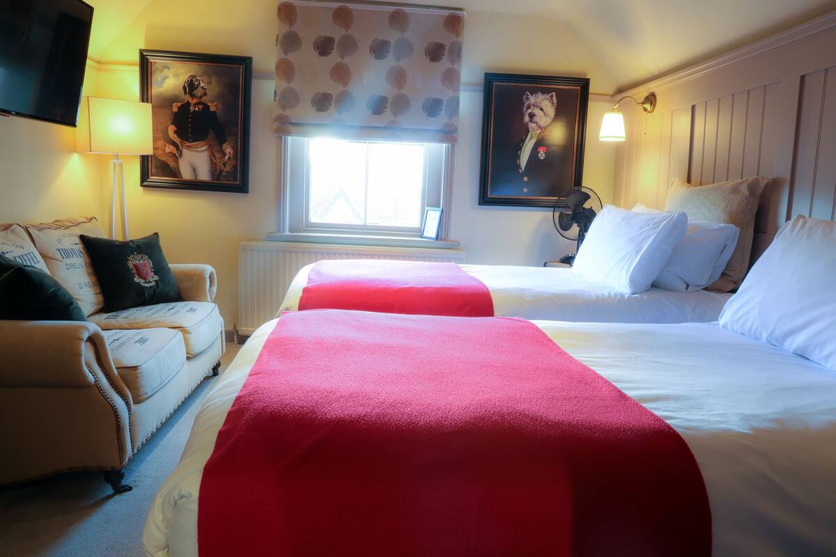 A hotel room with two beds, a sofa, and a window with blinds.