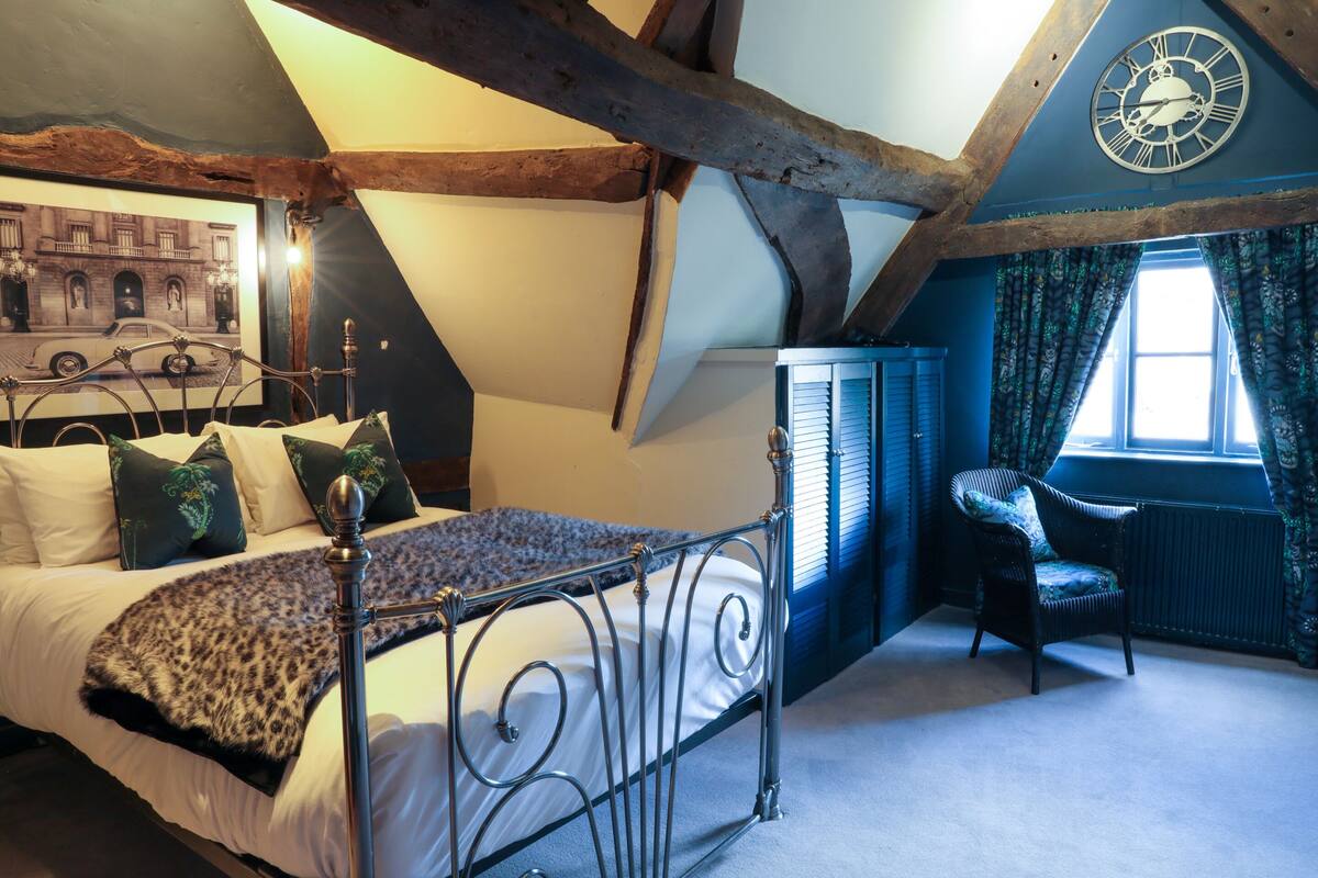 A bedroom with a bed, a chair, a clock, and a window.