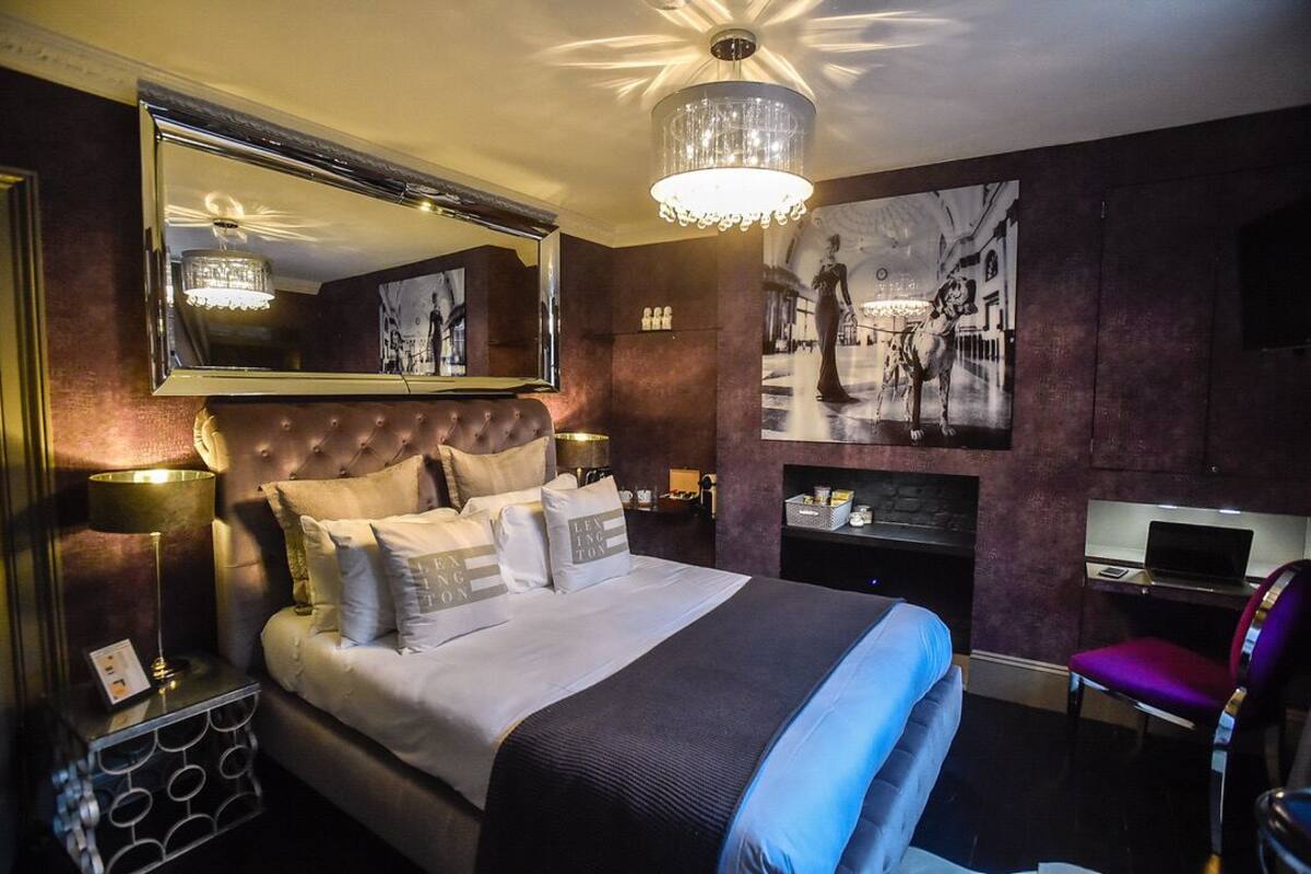 A bedroom with a large bed, a mirror, a chandelier, a desk, and a chair.