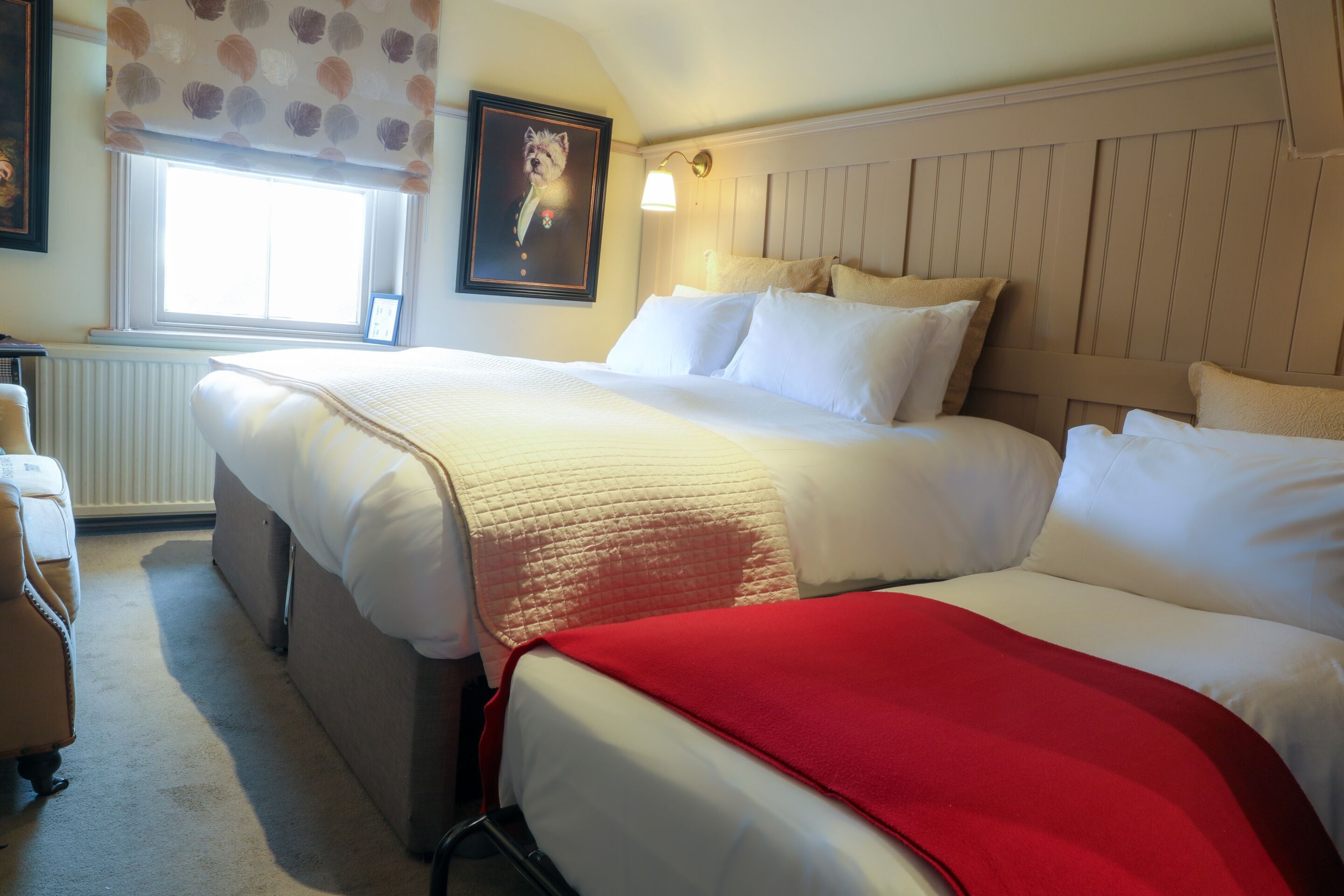Ett hotellrum med en stor säng, ett fönster med utsikt, en tavla på väggen och en röd pläd.