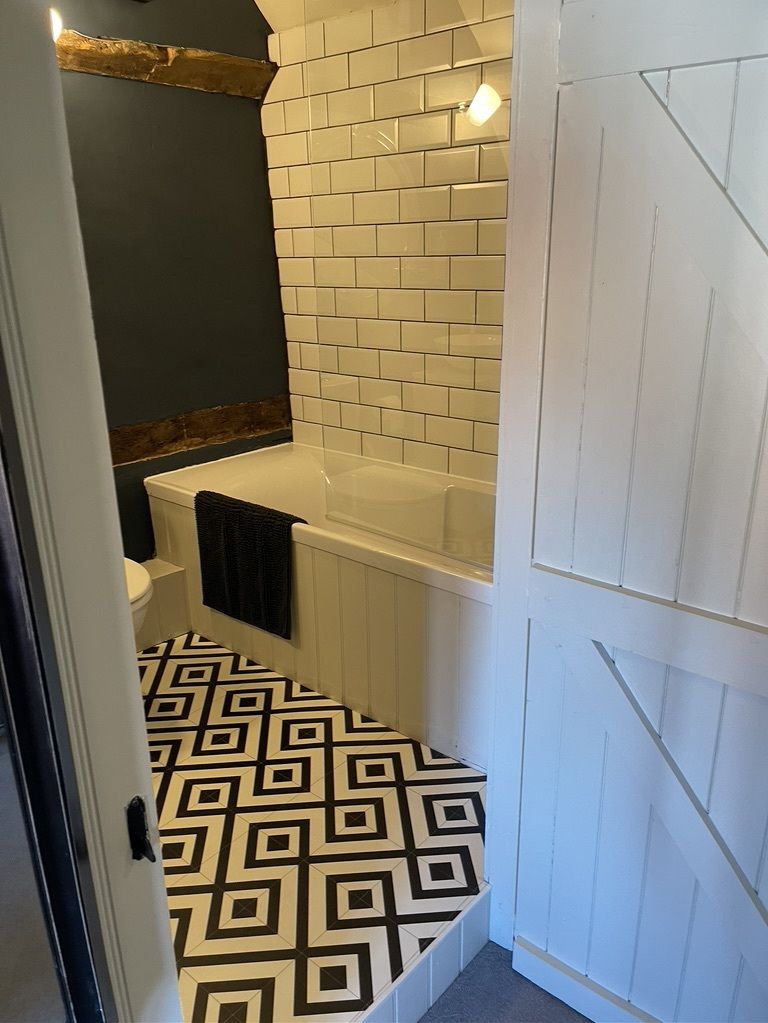 A bathroom with a white tiled wall, a black and white patterned floor, and a white bathtub.