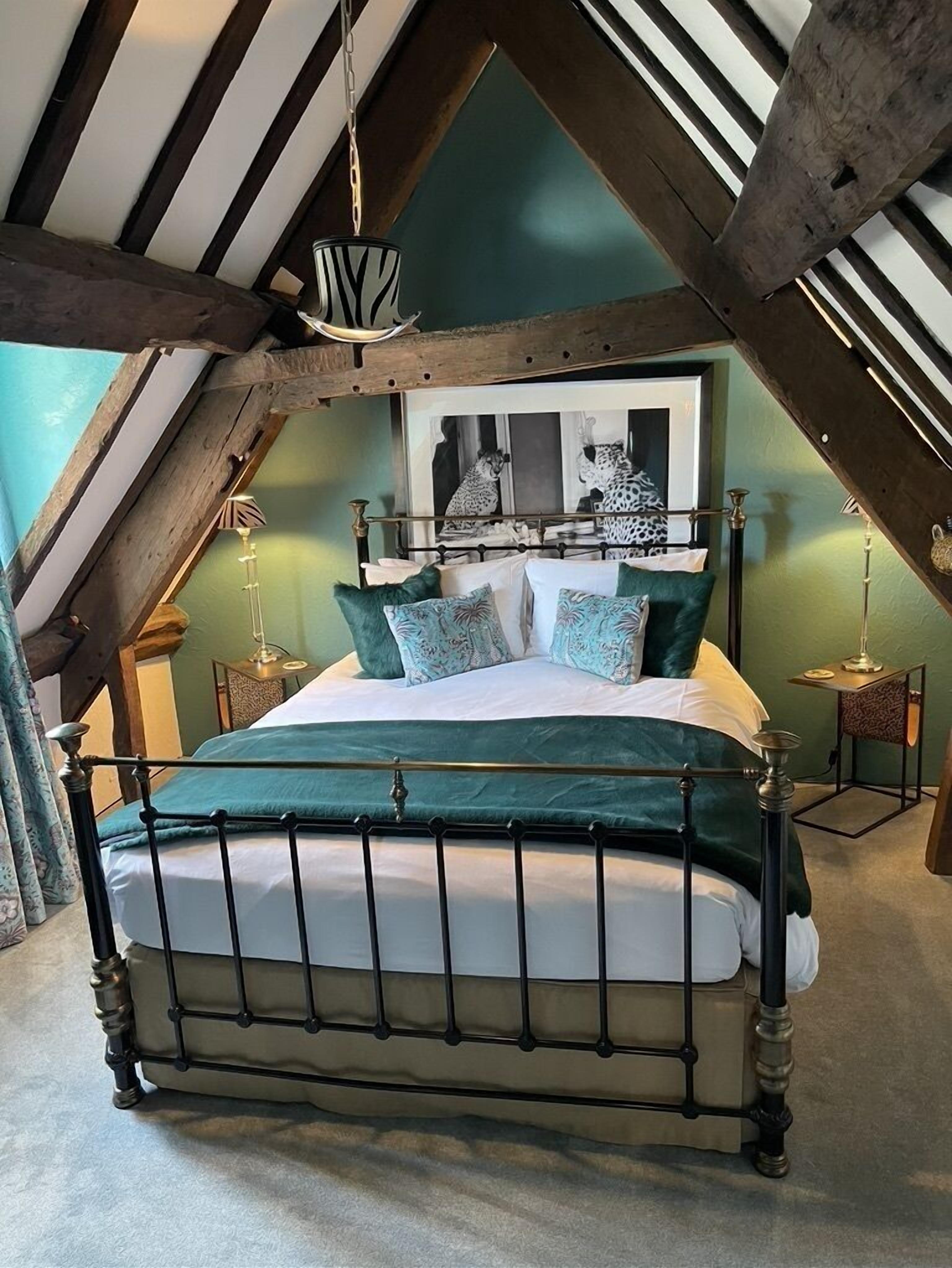 Une chambre avec un plafond haut, des poutres apparentes, un lit avec un cadre en métal et un tableau représentant un léopard.