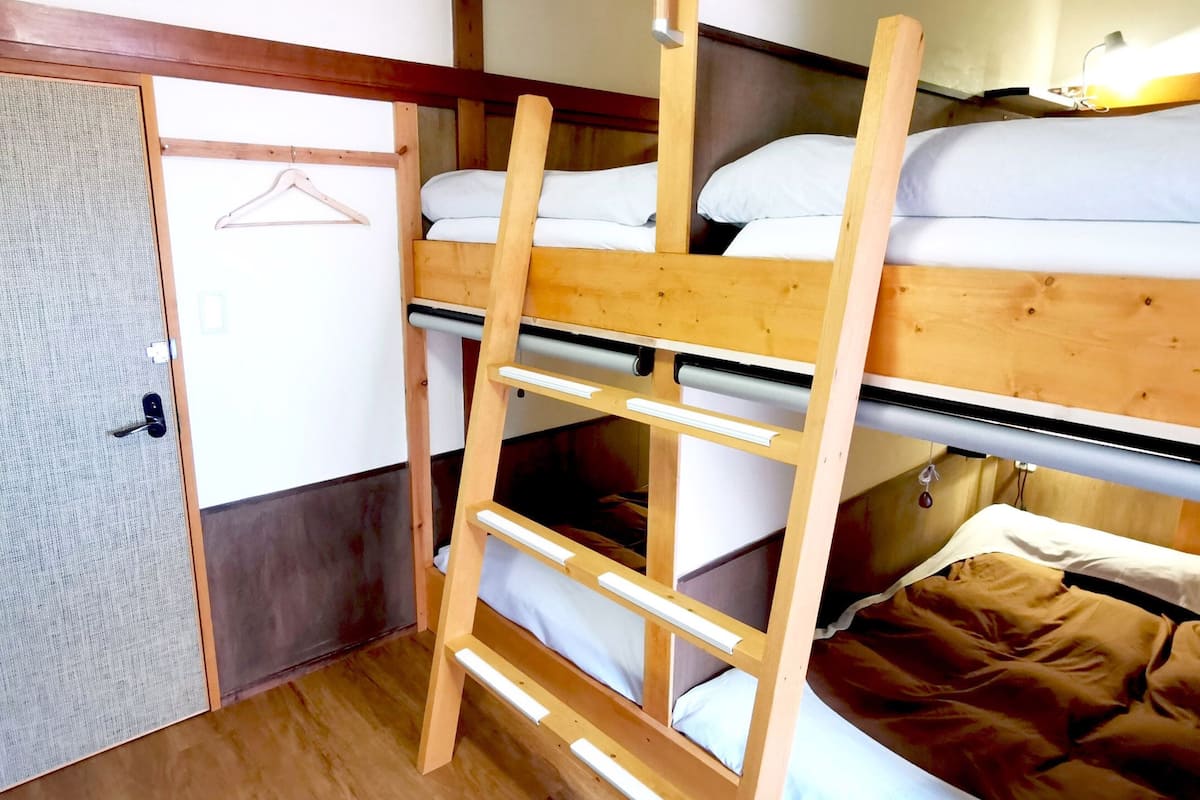 A bunk bed room with a wooden ladder, a hanging clothes rack, and a door.
