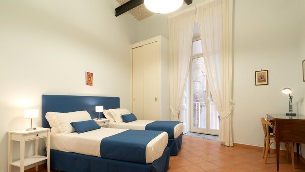 A hotel room with two beds, a desk, a chair, and a window with curtains. - Arbiter Apartments - L'amphora (Napoli)