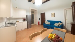 A compact kitchen with white cabinets, a stainless steel refrigerator, and a dining area with a table set for two. - Arbiter Apartments - L'amphora (Napoli)