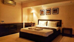 Una habitación de hotel con una cama grande, mesitas de noche, un aparador y un aire acondicionado instalado en la pared.