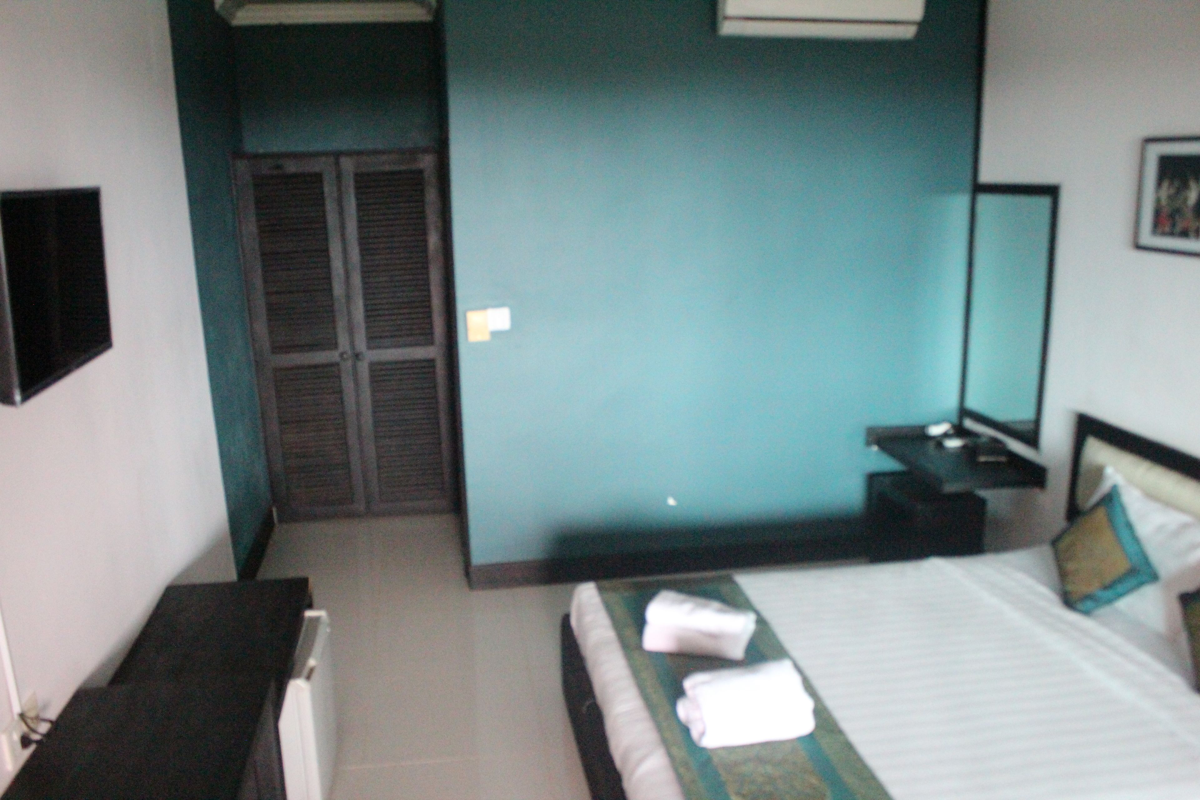A hotel room with a bed, a bedside table, a nightstand, a mirror, and a wardrobe.