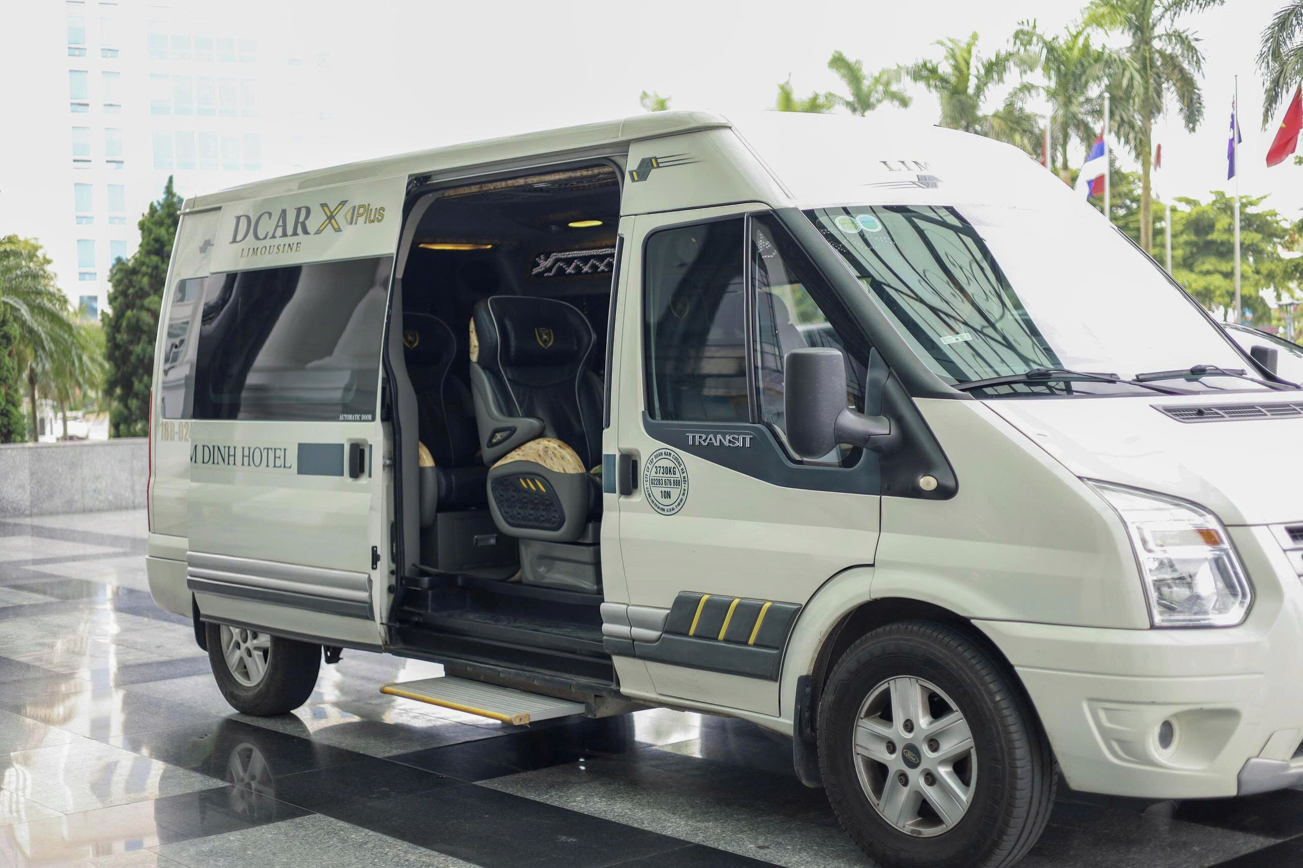 Ein weißer Van mit 'DCHARX Plus'-Branding, dem Schriftzug 'Dinh Hotel' und der Aufschrift 'TRANSIT' an der Seite.
