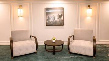 Dos sillones enfrentados con una mesita entre ellos, un cuadro enmarcado en la pared y luces fijadas a la pared.