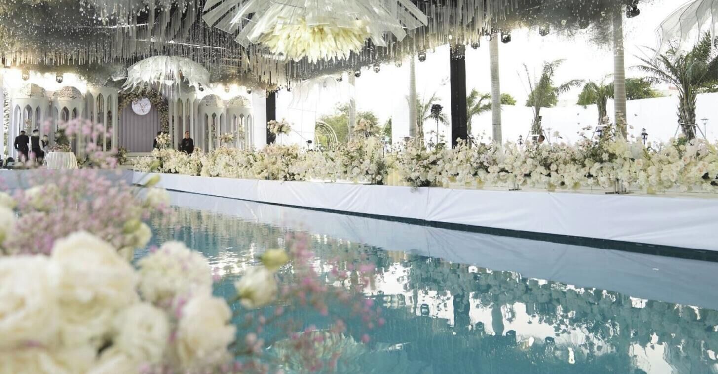 An indoor pool area with a white pool, surrounded by white floral arrangements and a decorative ceiling.