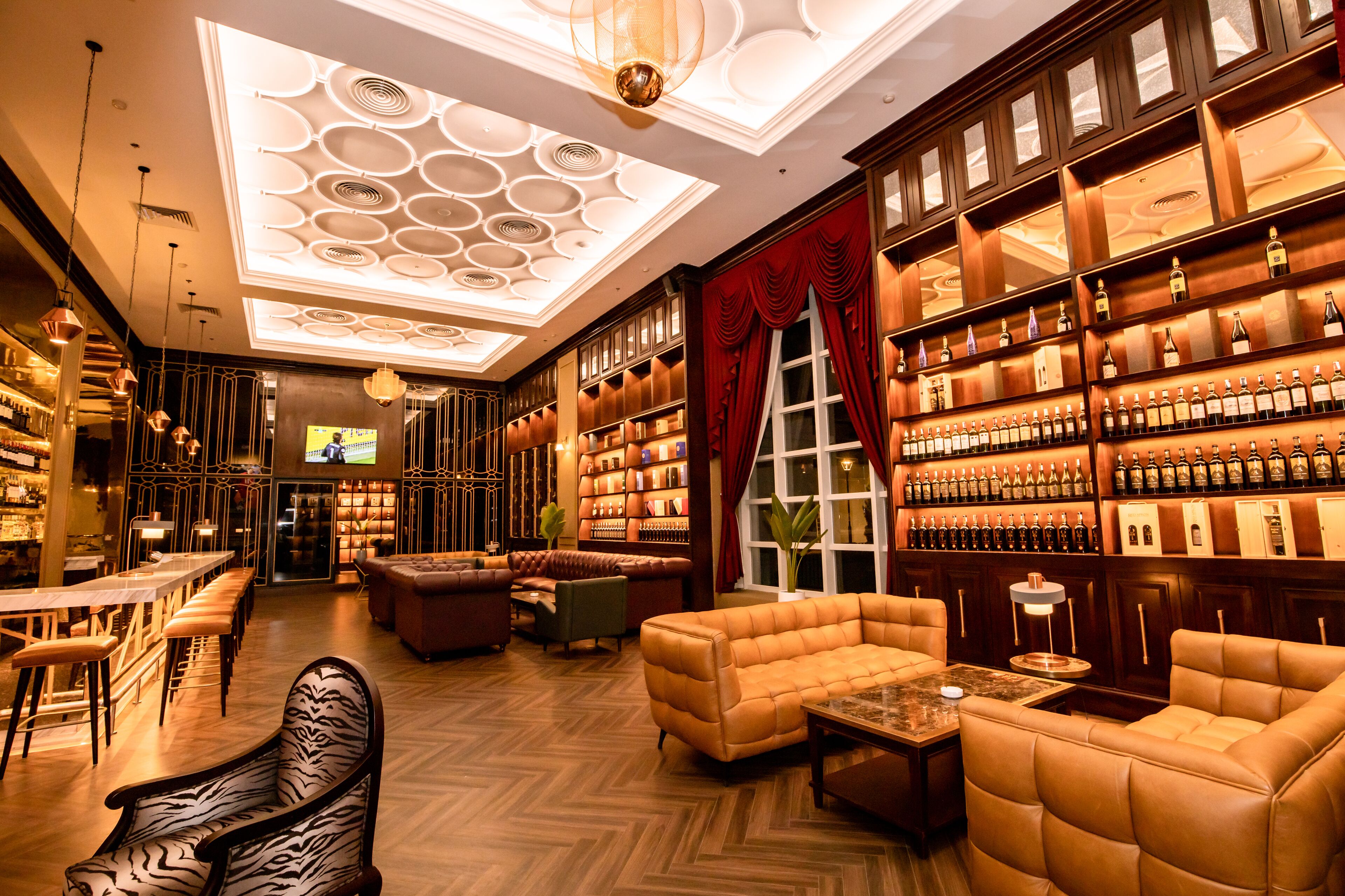 A bar area with wooden shelves of bottles, leather seating, and a patterned ceiling.