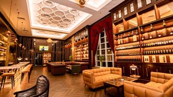 A bar area with wooden shelves of bottles, leather seating, and a patterned ceiling.