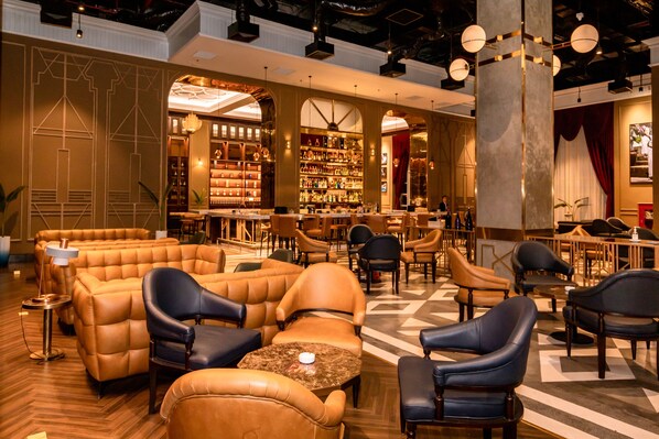 A spacious lounge area with leather sofas and armchairs, a bar with shelves of bottles, and a patterned floor.