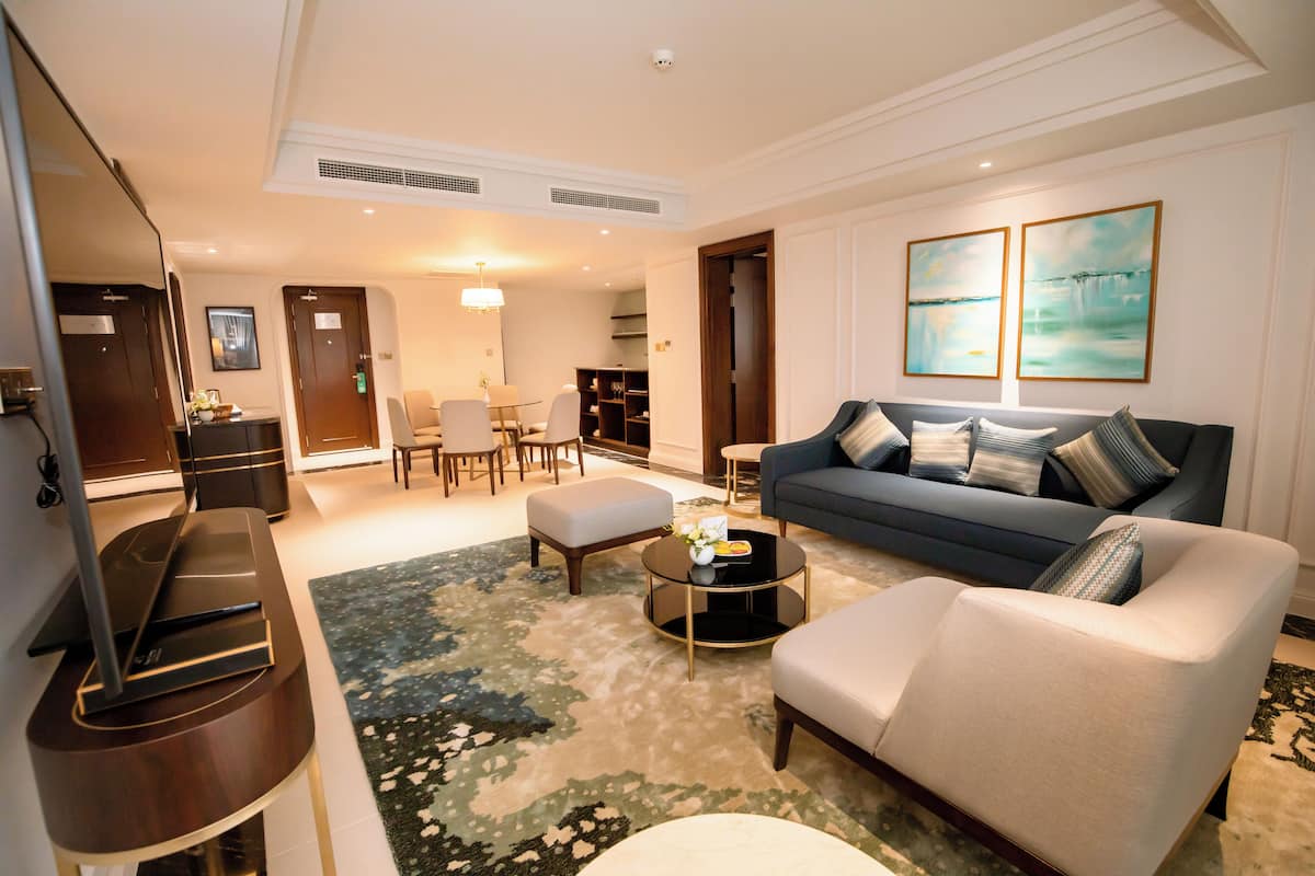 A modern living room with a sofa, coffee table, and TV stand. There is a dining area with chairs and a table in the background.