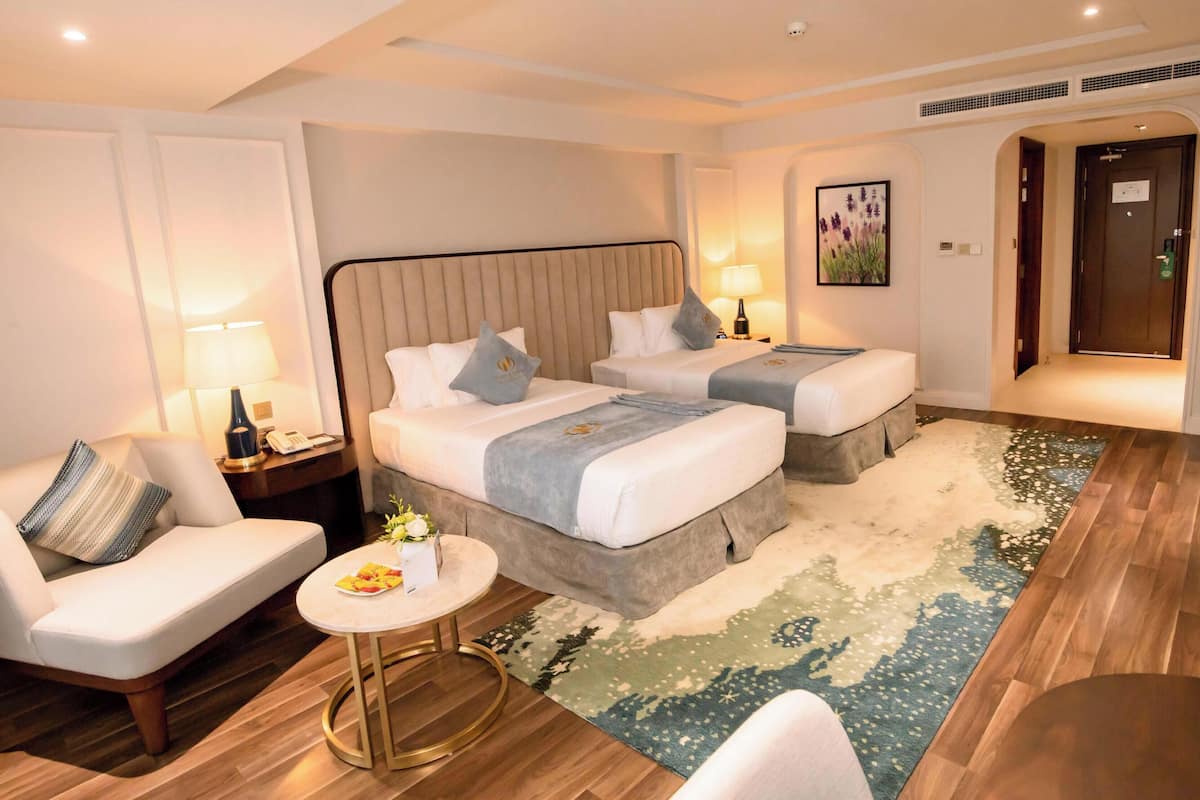 A hotel room with two beds, a sitting area with a chair, a small round table, and a decorative rug.