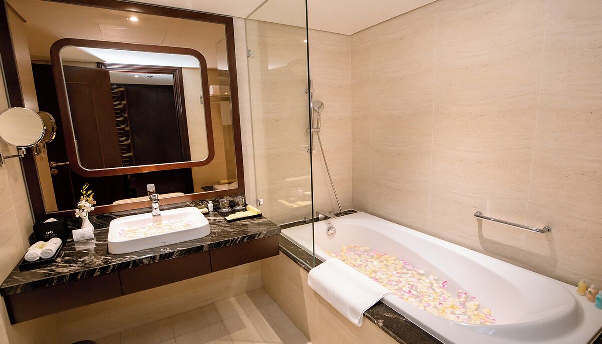 Un baño moderno con tocador de mármol, un espejo grande, una bañera con pétalos de rosa y un box de ducha de vidrio.