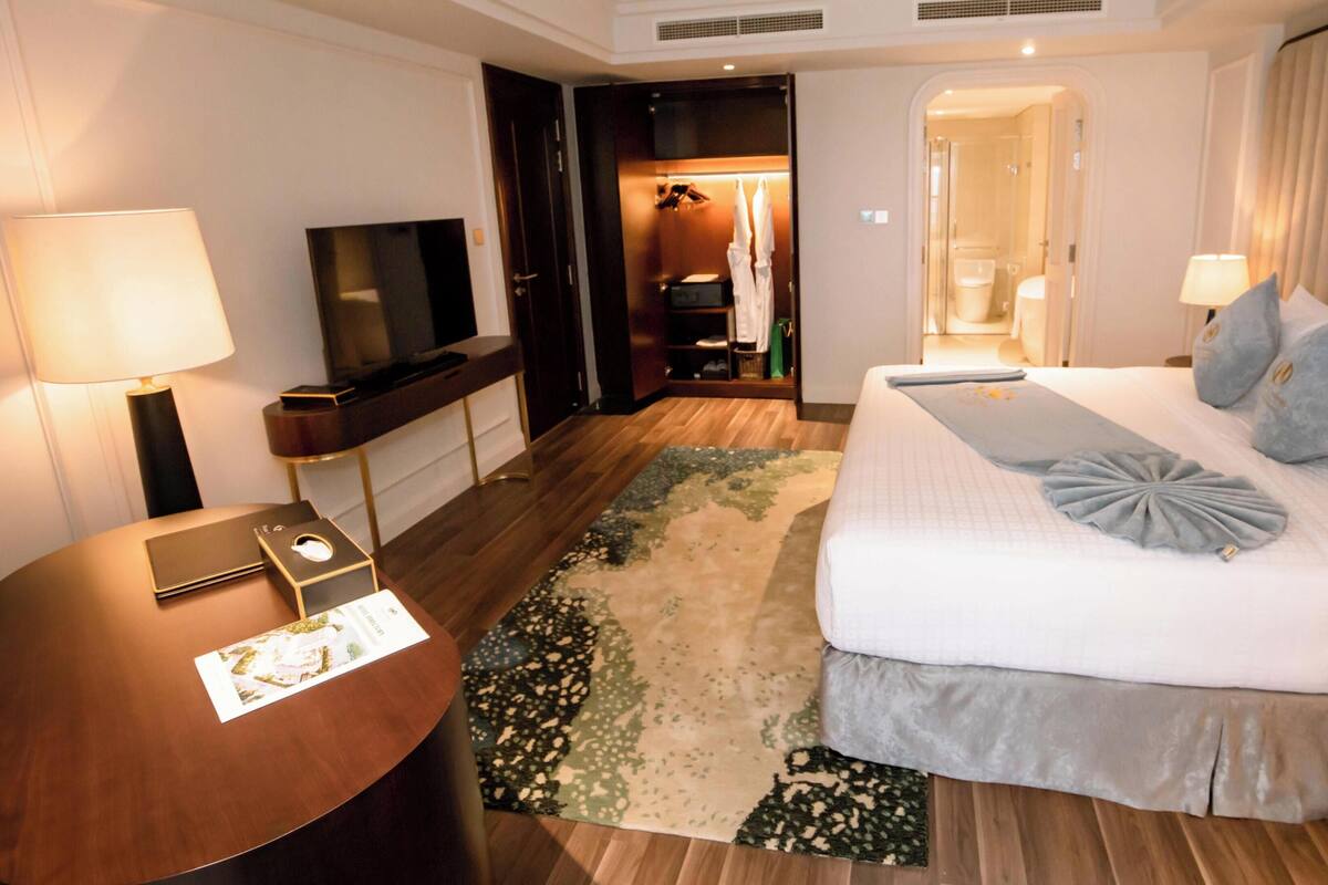 A hotel room with a bed, a TV, a desk, and a bathroom visible through an open door.
