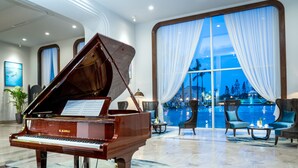 A grand piano in a spacious lobby with a large window overlooking a pool. - Nam Cuong Nam Dinh Hotel (Nam Dinh)