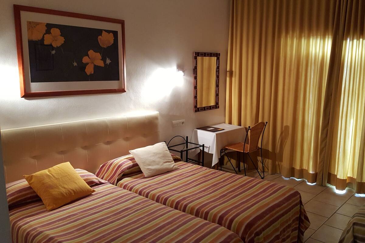 Habitació d'hotel amb dos llits, una taula de treball, una cadira i una finestra gran amb cortines.