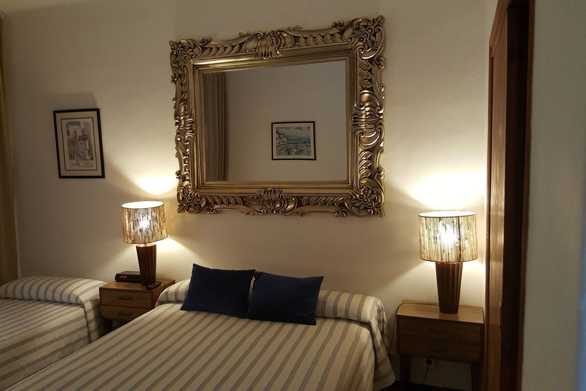 Habitació d'hotel amb dos llits individuals, un mirall gran i decoratiu, i dues làmpades de nit.