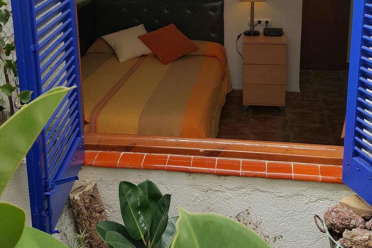 Un dormitori amb llit, taulella de nit, làmpada i un quadre al mur.